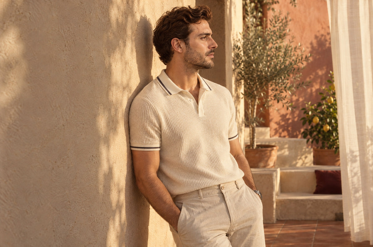 Man in a cream knit polo leaning against a sunlit terrace wall