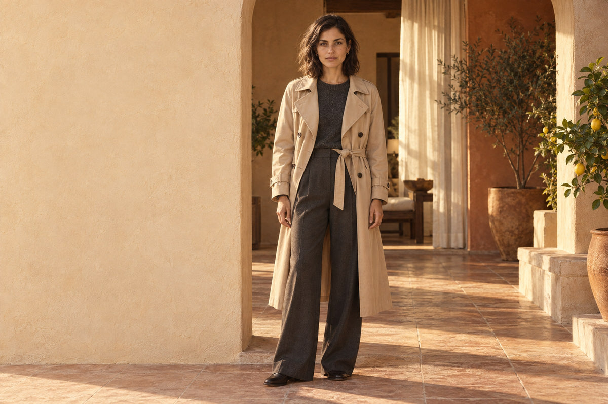 Woman in a belted sand trench coat standing in a sunlit stone archway